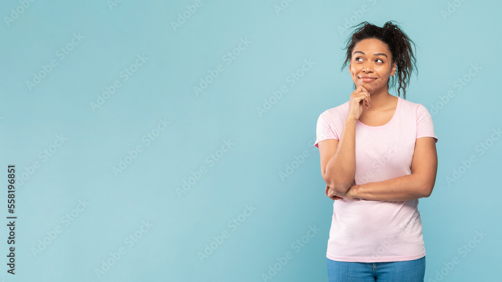 Thoughtful african american woman thinking and looking aside at free space, posing standing on blue studio background Thoughtful african american woman thinking and looking aside at free space, posing standing on blue studio background