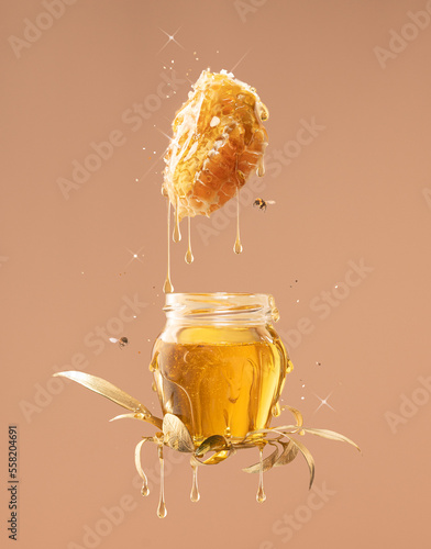 Honey in a jar with flying bees and dripping honeys from natural honeycombs in freeze motion.Healthy Food levitation on beige background.Studio shot.