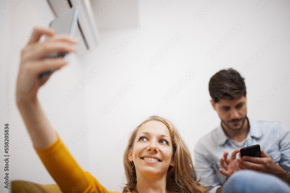 girl at home taking selfie on her smart phone. boyfriend in the backgroung paying no attention. girl at home taking selfie on her smart phone. boyfriend in the backgroung paying no attention.