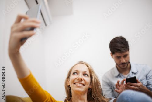 girl at home taking selfie on her smart phone. boyfriend in the backgroung paying no attention.