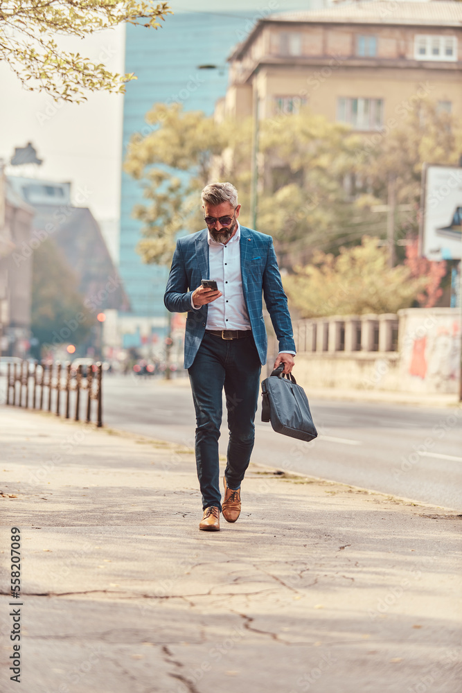 A senior businessman in a blue suit in an urban environment using a smartphone