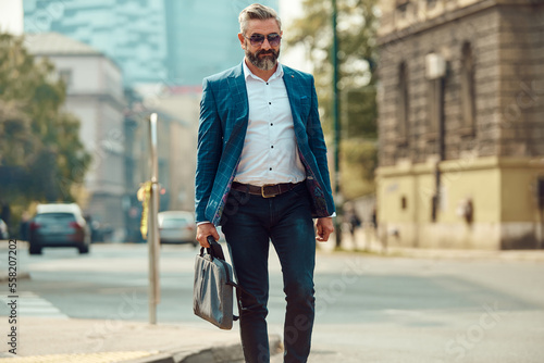 A senior businessman in a blue suit with a briefcase walking through the city