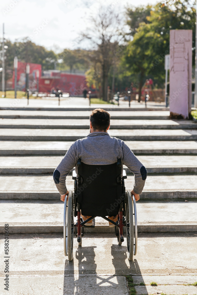Obraz premium Man in a wheelchair faced with an accessibility problem on the stairs in the park.