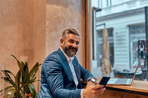 Modern senior businessman sitting in cafe and using laptop and smartphone