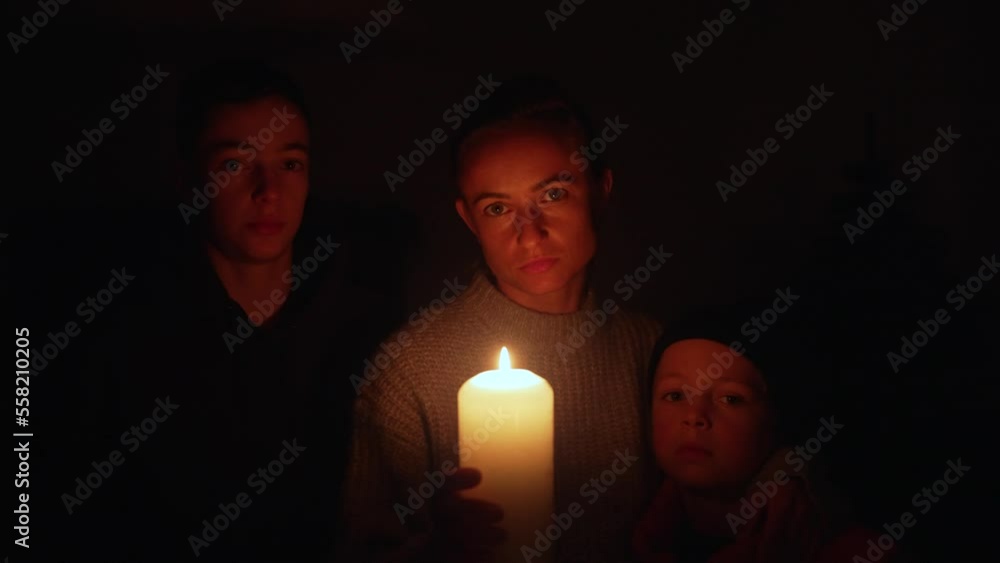 Woman with two children waiting at home by the candles during the blackout. Mother with her sons under candle lights during a balckout due to energy crisis in Ukraine. Woman with two children waiting at home by the candles during the blackout. Mother with her sons under candle lights during a balckout due to energy crisis in Ukraine.