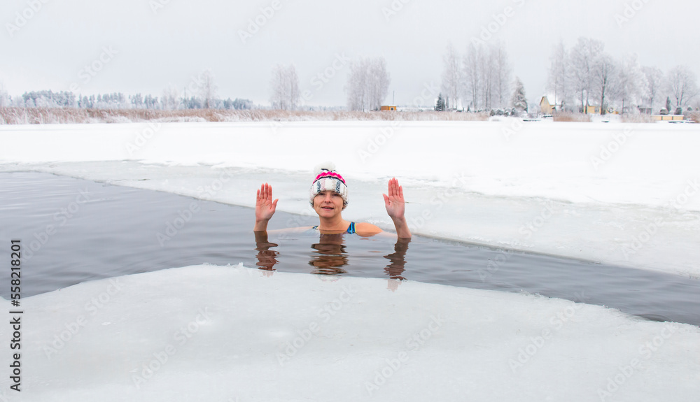 A seasoned strong woman in an ice-cold water hole in a lake, dipping in ...