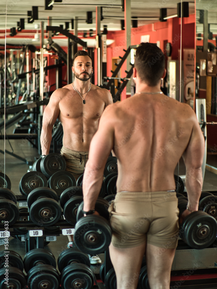 Naklejka premium Muscular, shirtless male bodybuilder working out in gym