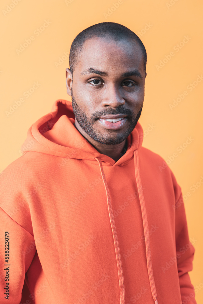 The portrait of a dark-skinned man in an orange hoodie, Black guy fashion. Orange background. The portrait of a dark-skinned man in an orange hoodie, Black guy fashion. Orange background.