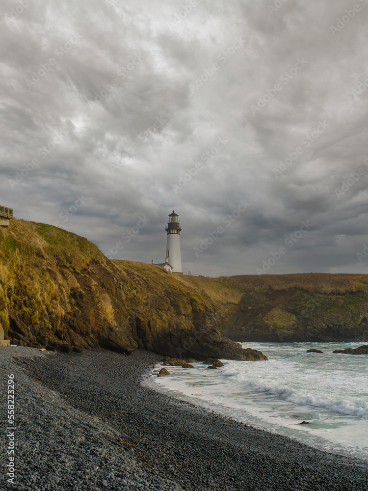 Gloomy landscape. A lone lighthouse on a high hilly shore. Sea waves crash on the shore. There are gray storm clouds in the sky. Desert place. The beauty and majesty of nature.