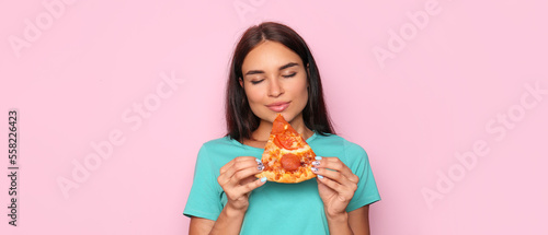 Happy young woman with slice of delicious pizza on pink background