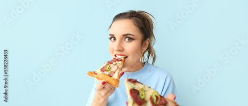 Portrait of beautiful young woman eating fresh pizza on light blue background