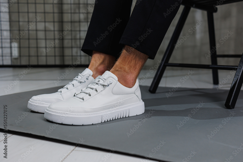 Male legs in black pants and white casual sneakers. Men's fashionable shoes