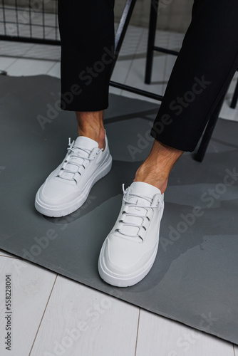 Male legs in black pants and white casual sneakers. Men's fashionable shoes