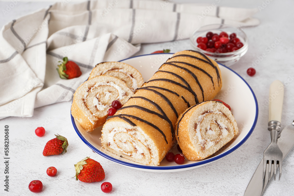 Plate with delicious sponge cake roll, fresh berries, cutlery and napkin on white table Plate with delicious sponge cake roll, fresh berries, cutlery and napkin on white table