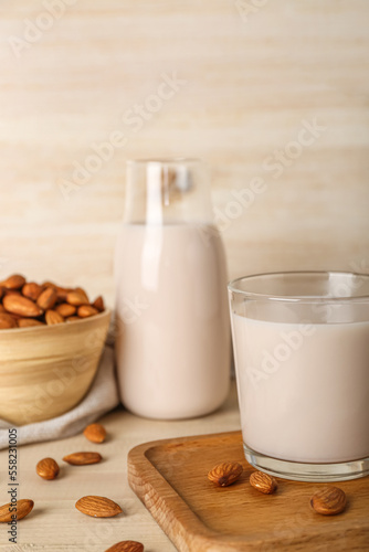 Board with glass of healthy almond milk and nuts on wooden background, closeup