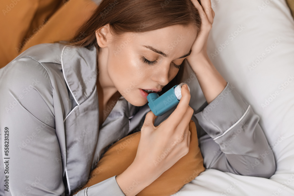 Sick young woman with inhaler in bed