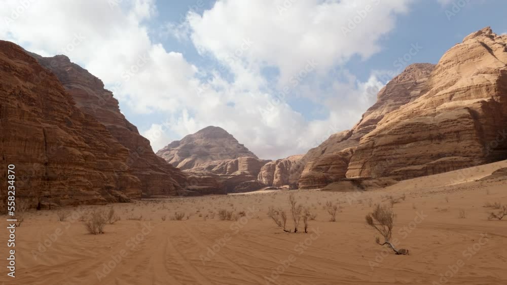 Panoramic view of Wadi Rum desert in Jordan with clouds moving over flat sand landscape with mountains in background, 