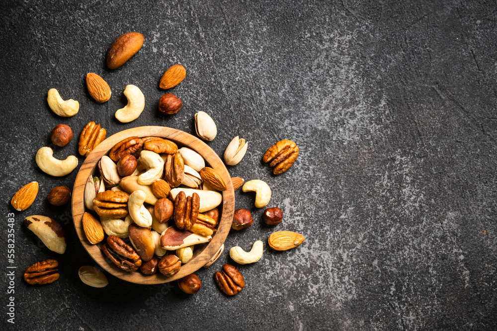 Assortment of nuts in wooden bowl on dark stone table. Cashew, hazelnuts, almonds, brazilian nuts and pecans. Top view with copy space. Assortment of nuts in wooden bowl on dark stone table. Cashew, hazelnuts, almonds, brazilian nuts and pecans. Top view with copy space.