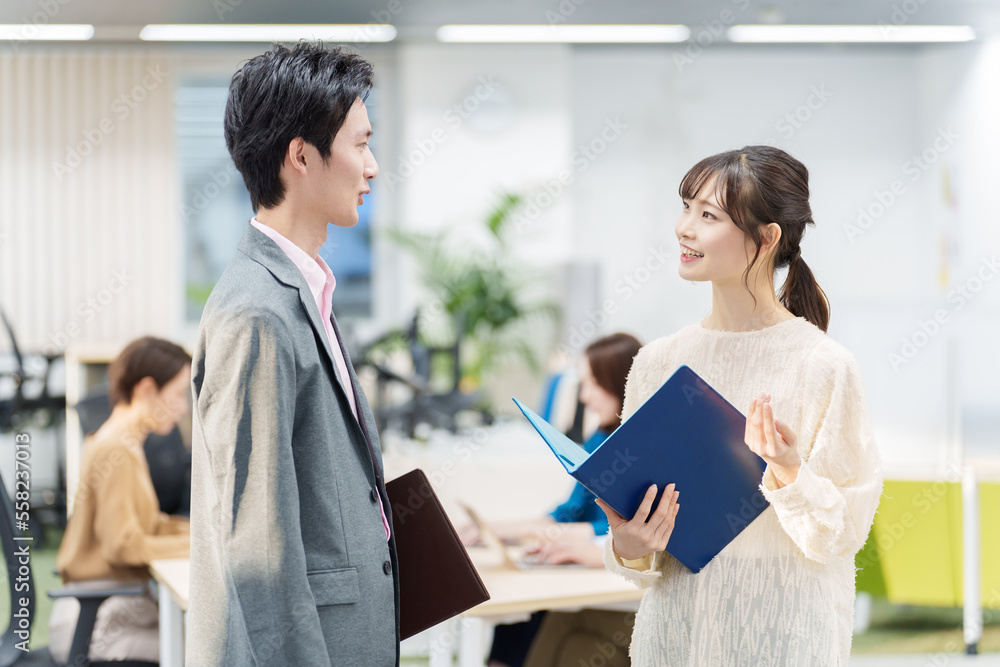 オフィスで立ち話をする若い男女 オフィスで立ち話をする若い男女