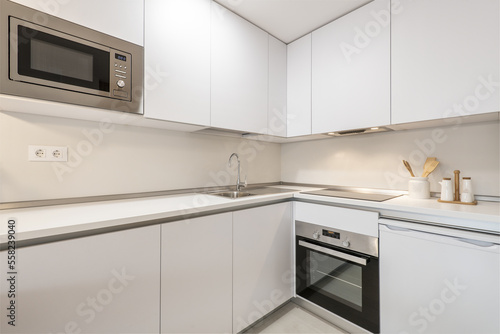 Corner of a fitted kitchen with contemporary decoration with handleless doors and integrated appliances and a smooth white worktop