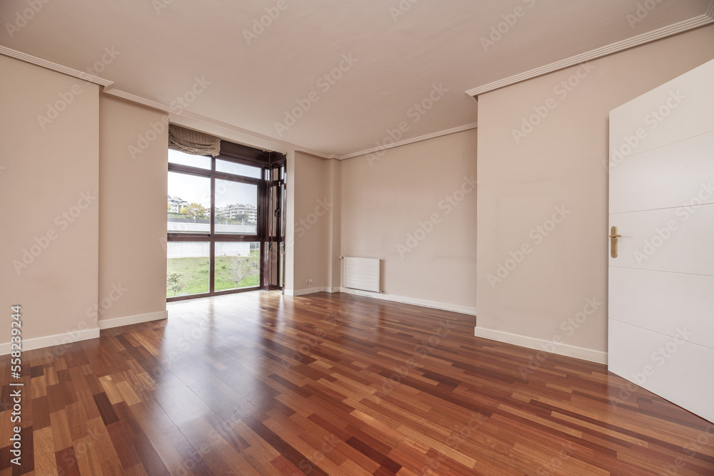 Large empty living room of a house with wooden floors, built-in bookshelf and a glass window with a view Large empty living room of a house with wooden floors, built-in bookshelf and a glass window with a view
