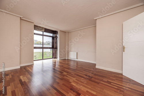 Large empty living room of a house with wooden floors, built-in bookshelf and a glass window with a view