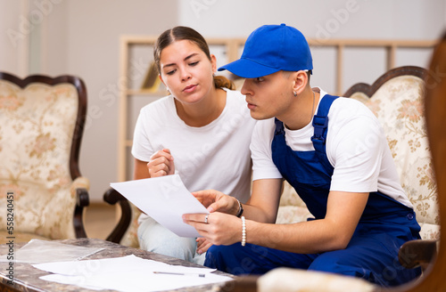 Owner of partment and the young builder sign documents while sitting on sofa in the living room photo