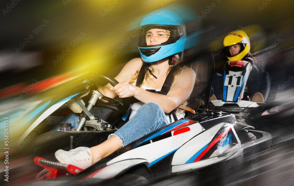 sportive adulr woman in helmet driving car for karting with other people in sport club indoor