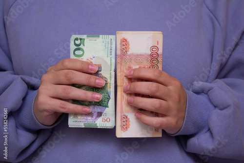 Currency exchange. Paper bill of 5000 rubles and 50 GEL bills in Female hand. Russian ruble and Georgian lari. Woman in purple long sleeve hoodie is holding stack of cash. Money for tourism, trip. Pay