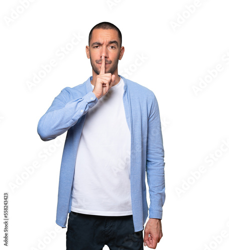 Serious young man asking for silence gesturing with his finger
