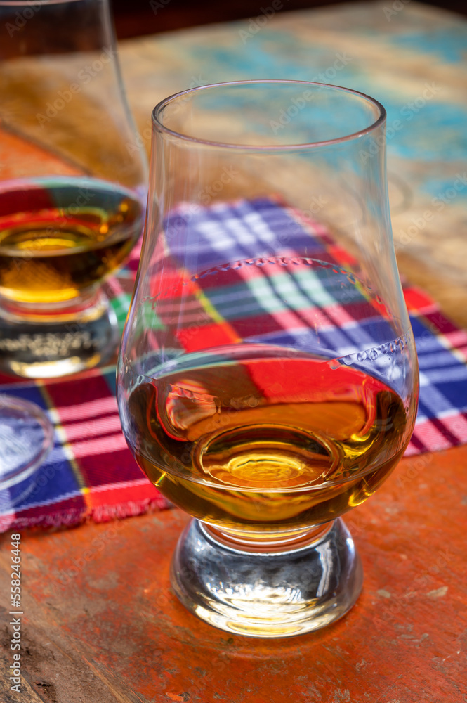 Tulip-shaped tasting glass with dram of Scotch single malt or blended whisky on wooden table with tartan Tulip-shaped tasting glass with dram of Scotch single malt or blended whisky on wooden table with tartan