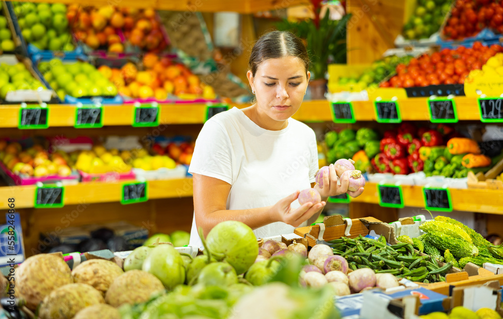Focused girl buyer who came to the vegetable store for shopping, chooses fresh products to buy them