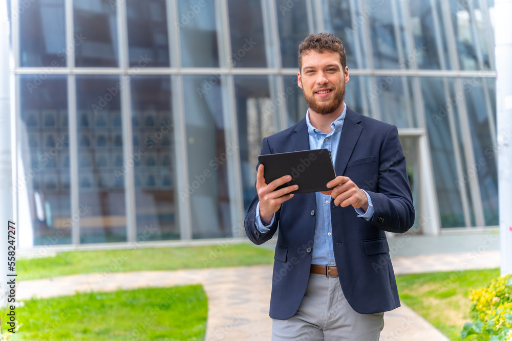 Young male businessman or entrepreneur outside the office, walking with a tablet in his hand Young male businessman or entrepreneur outside the office, walking with a tablet in his hand