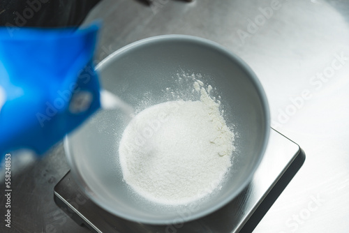Top view of white sugar being poured intro a bowl placed on a metal stand. Blurred foreground. High quality photo