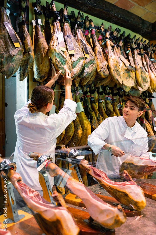 Butcher shop owner and assistant sell Spanish traditional ham