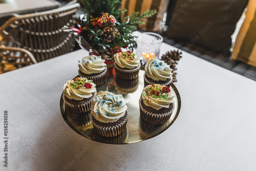 Bakery and cafe studio. Plate with tasty muffins with white frosting and colorful sprinkles. Christmas decorations. High quality photo