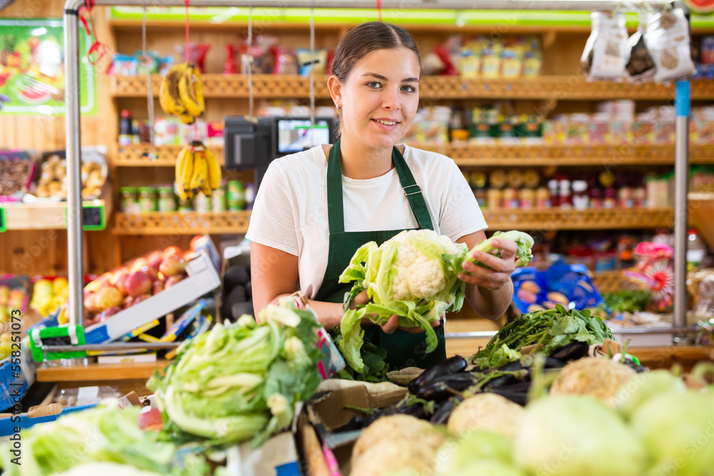 Portrait of joyful female merchandiser with cauliflower in hands at grocery supermarket