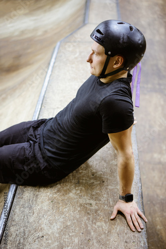 Side view of skater in protective helmet sitting on ramp in skate park 