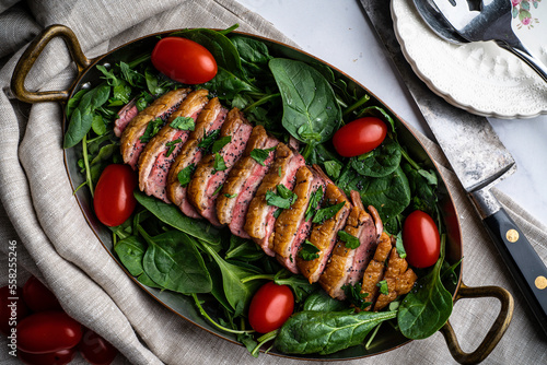 Pan-roasted duck breast served with spinach, arugula, and grape tomatoes. Garnished with parsley and black poppy seeds.