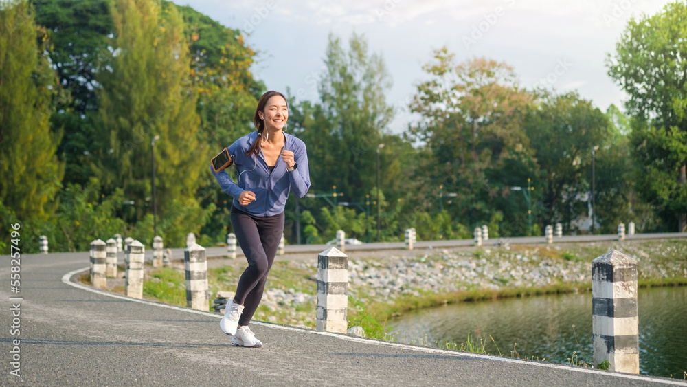 Horizontal shot of athletic woman in sportswear jogging in park during sunset.
