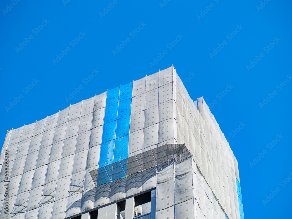 Building under construction wrapped blue and white protection safety net. Building under construction wrapped blue and white protection safety net.
