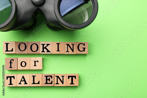 Staff recruitment concept. Phrase Looking For talent made of wooden cubes and binoculars on green background, flat lay. Space for text