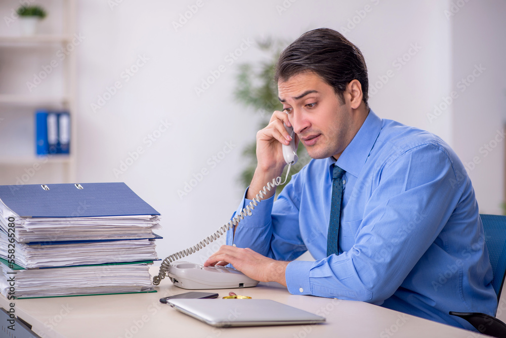 Young male employee and too much work in the office Young male employee and too much work in the office