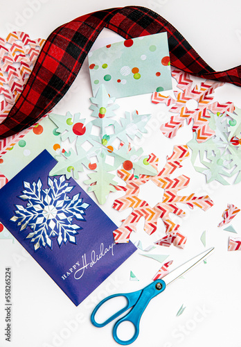 Papercraft snowflakes with a Christmas card and decorative ribbon on white.