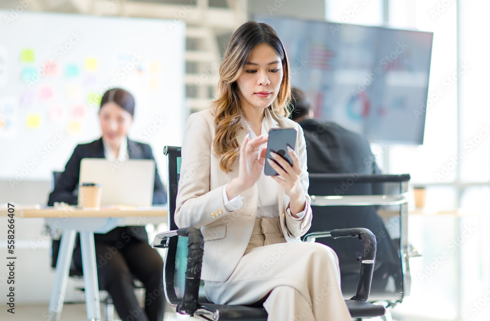 Obraz premium Millennial Asian young professional successful female businesswoman in formal suit high heels sitting smiling posing on chair listening to lecturer with male colleague in company office meeting room