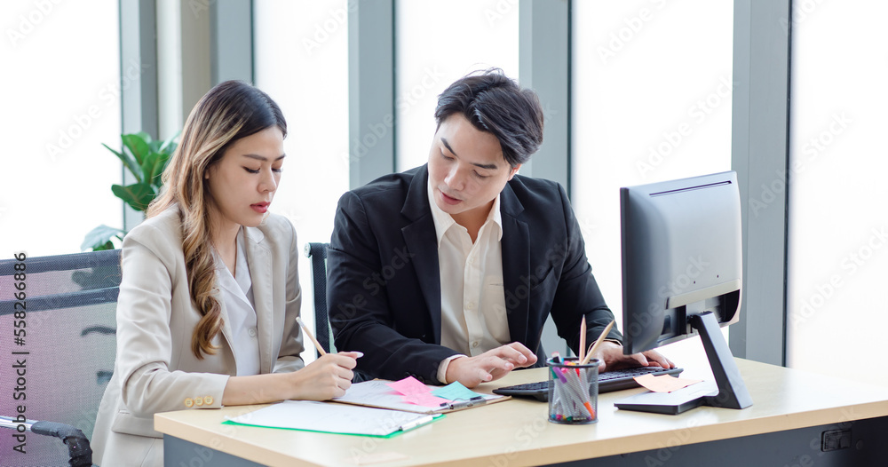 Millennial Asian professional successful female businesswoman mentor in formal suit sitting writing data helping male businessman trainee working with paperwork document in company office workstation Millennial Asian professional successful female businesswoman mentor in formal suit sitting writing data helping male businessman trainee working with paperwork document in company office workstation