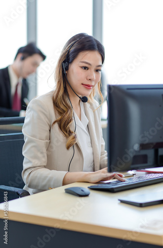 Closeup shot of Millennial Asian young professional successful female businesswoman secretary operator in formal suit with stereo headset microphone sitting working talking with customer in office
