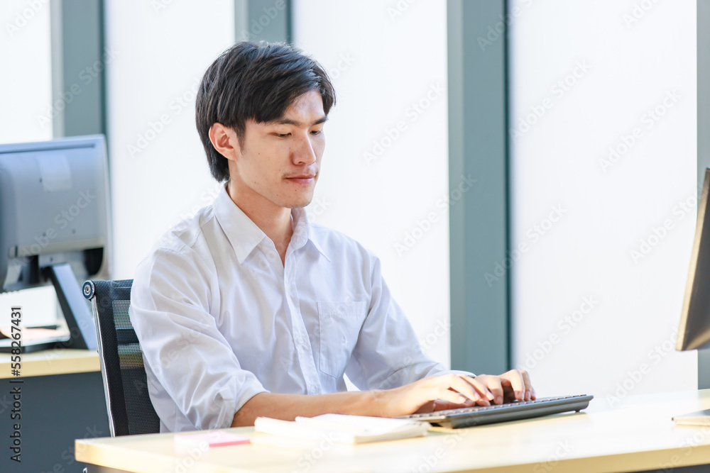 Portrait shot of Millennial Asian young professional successful male businessman sitting smiling looking at camera working typing with computer keyboard in company office workstation. Portrait shot of Millennial Asian young professional successful male businessman sitting smiling looking at camera working typing with computer keyboard in company office workstation.