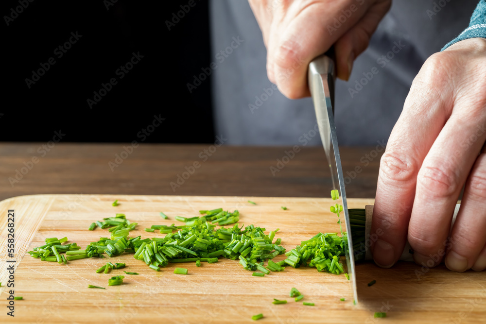 A chef slicing fresh chives on a wooden cutting board. A chef slicing fresh chives on a wooden cutting board.