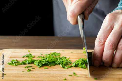 A chef slicing fresh chives on a wooden cutting board.